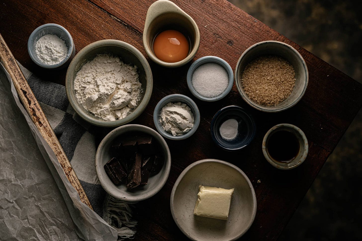 Key ingredients for a small-batch chocolate chip cookie recipe, including baking soda, vanilla, sugar, and egg yolk. brown sugar, unsalted butter, and chocolate chunks are displayed in bowls.