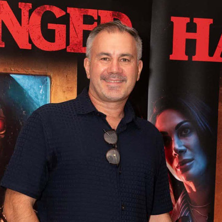 Simon Cluett at a screening of supernatural horror film Harbinger, standing in front of posters featuring the film’s sinister fortune-telling machine and the tagline “Death is on the cards.” Simon Cluett at a screening of supernatural horror film Harbinger, standing in front of posters featuring the film’s sinister fortune-telling machine and the tagline “Death is on the cards.”