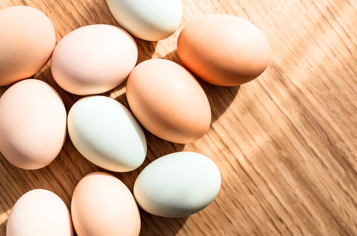 A cluster of brown and cream eggs resting on a wooden surface, with gentle natural light creating soft shadows and a warm, rustic feel. A cluster of brown and cream eggs resting on a wooden surface, with gentle natural light creating soft shadows and a warm, rustic feel.