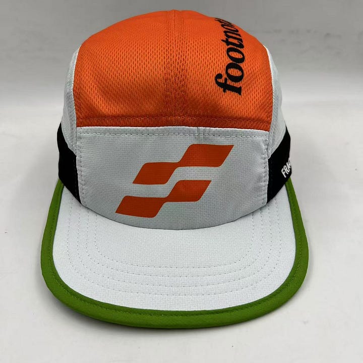 Images of the Footnotes Fractel hat including the orange logo on the front panel and underneath the brim. The newsletter's name is typed on the top of the hat and a green stripe accents the brim.