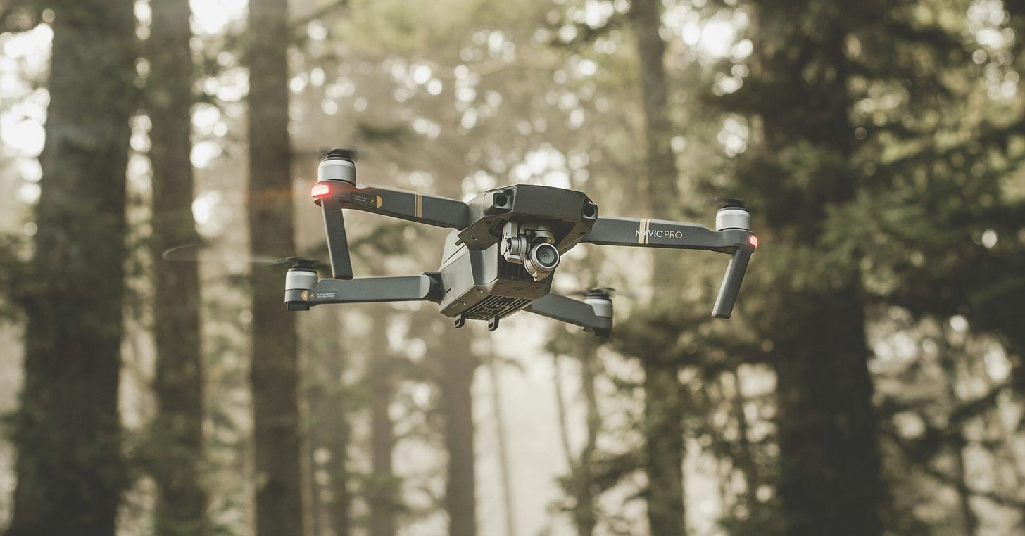 A photo of a drone hovering in the forest at daytime. A photo of a drone hovering in the forest at daytime.