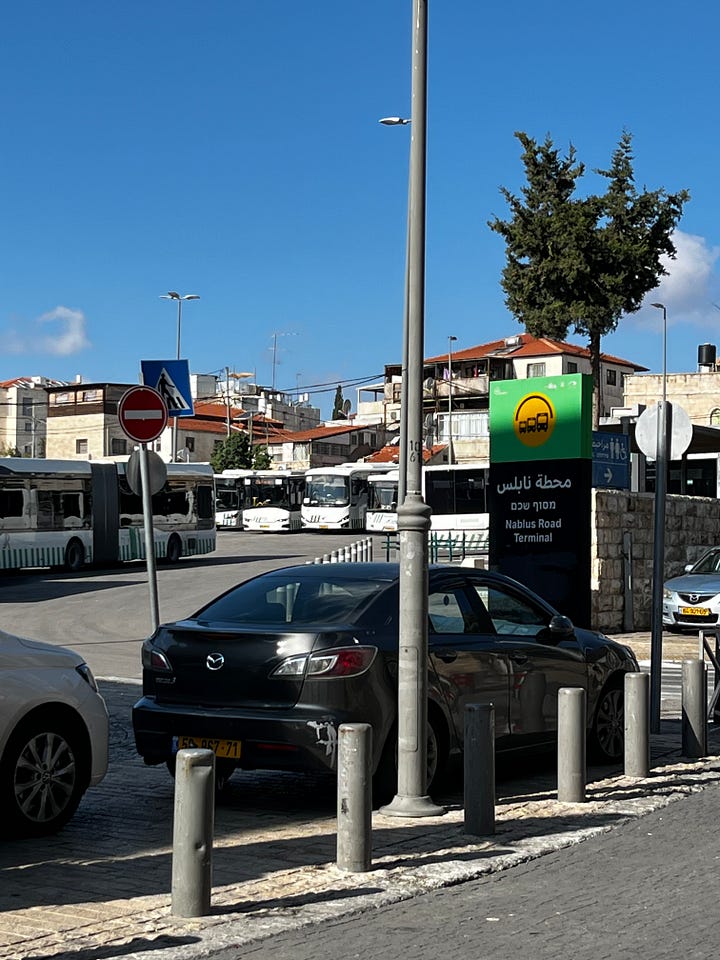 Left: Close-up of the Nablus Road Terminal sign mounted on a green post. The sign displays the terminal name in three languages: Arabic (محطة نابلس) at top, Hebrew (מסוף שכם) below it, and English ("Nablus Road Terminal") at the bottom, alongside a yellow bus system logo on a green background. Multiple white buses are visible in the terminal behind the sign. Jerusalem stone buildings and a clear blue sky fill the background. Right: A wide view of the Nablus Road Terminal from street level. A large Jerusalem stone church with a cross is visible on the left. The terminal sign and bus shelters occupy the left middle ground. An open roundabout with a pedestrian crossing occupies the center. Buses are pulled into covered stalls on the right. Blue wayfinding signs in Arabic are visible. Trees and stone buildings frame the scene under a partly cloudy sky.