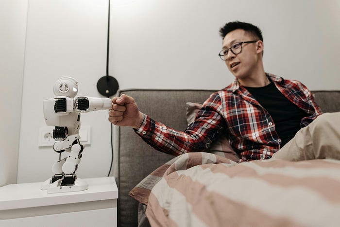 A man sitting in bed while fist bumping a tiny robot