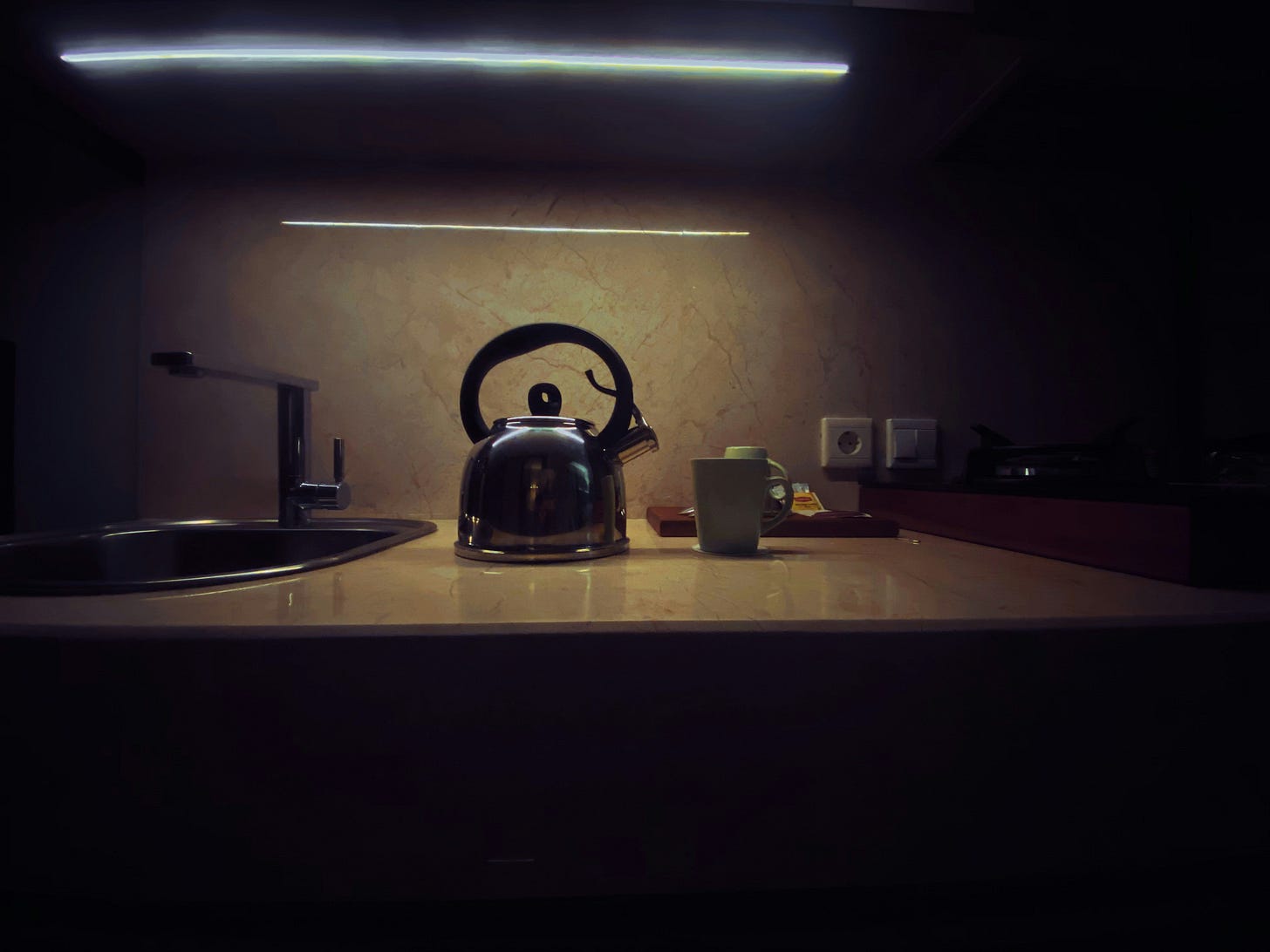 Black tea kettle resting on a wooden table beside soft morning light. Image by Kahfira Krisna