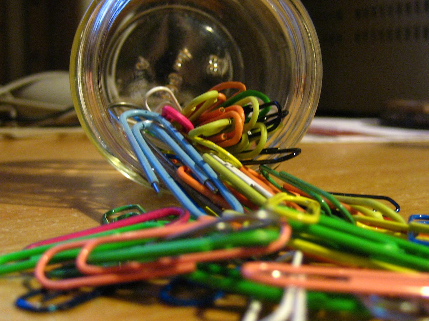 Multicolored paperclips spilling out of a jar onto a table