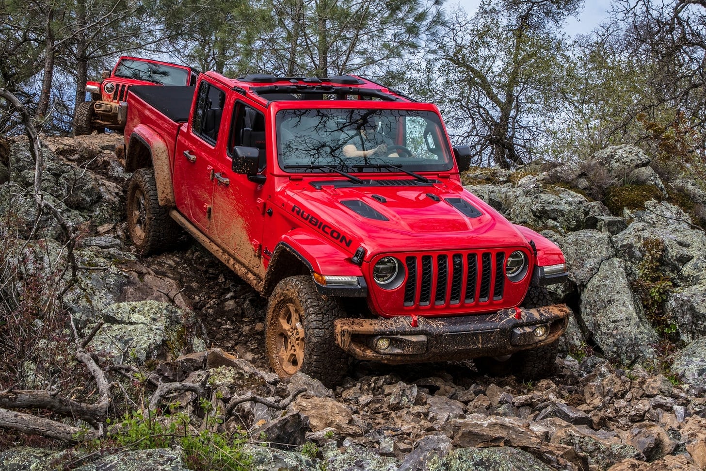 A red Jeep Gladiator Rubicon makes its way down a rocky, muddy slope in California.
