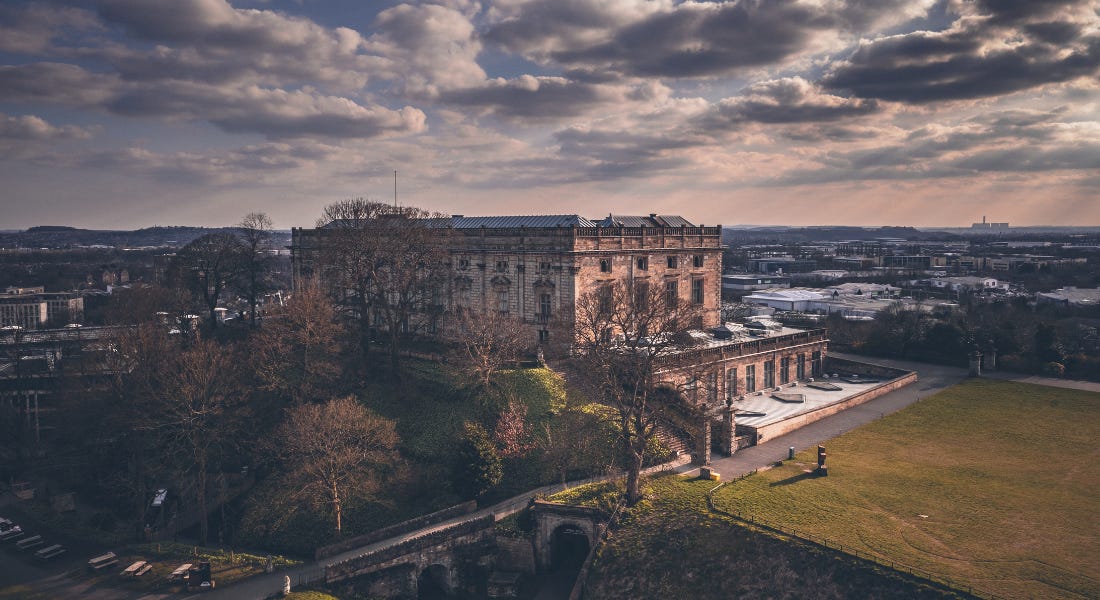 A castle - Nottingham Castle - on a hill with trees and a city skyline around it