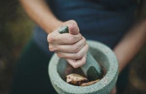 a woman crushing fresh herbs in a bowl