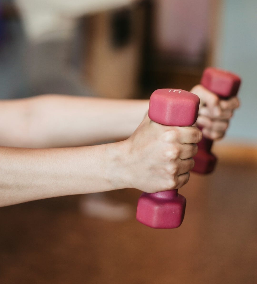 person holding pink and white dumbbells