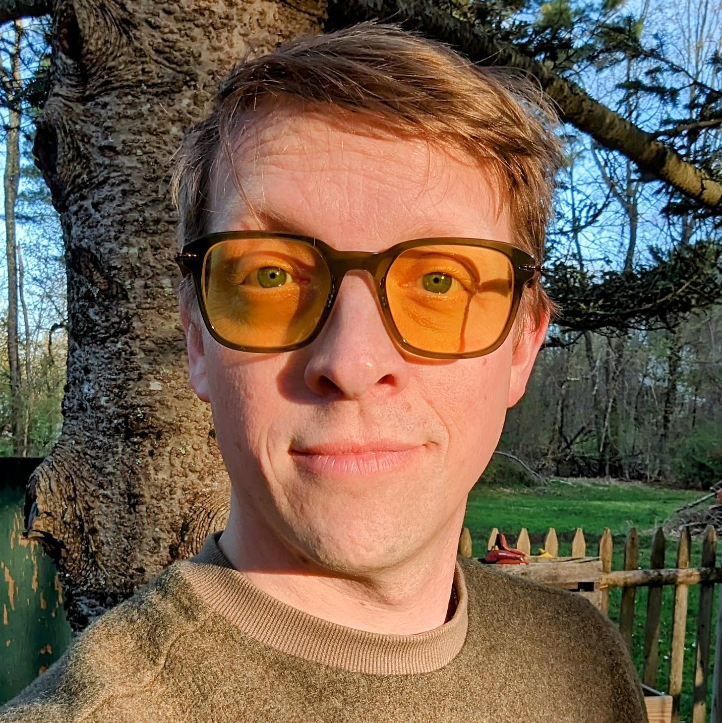 A photo of the author, cropped from shoulders up. He is wearing yellow-tinted glasses and smiling slightly, standing in front of a large pine tree inside a picket fence visible in the background. Beyond the fence there is a grassy yard and wooded area beyond that. The blue sky is visible through tree branches. A photo of the author, cropped from shoulders up. He is wearing yellow-tinted glasses and smiling slightly, standing in front of a large pine tree inside a picket fence visible in the background. Beyond the fence there is a grassy yard and wooded area beyond that. The blue sky is visible through tree branches.