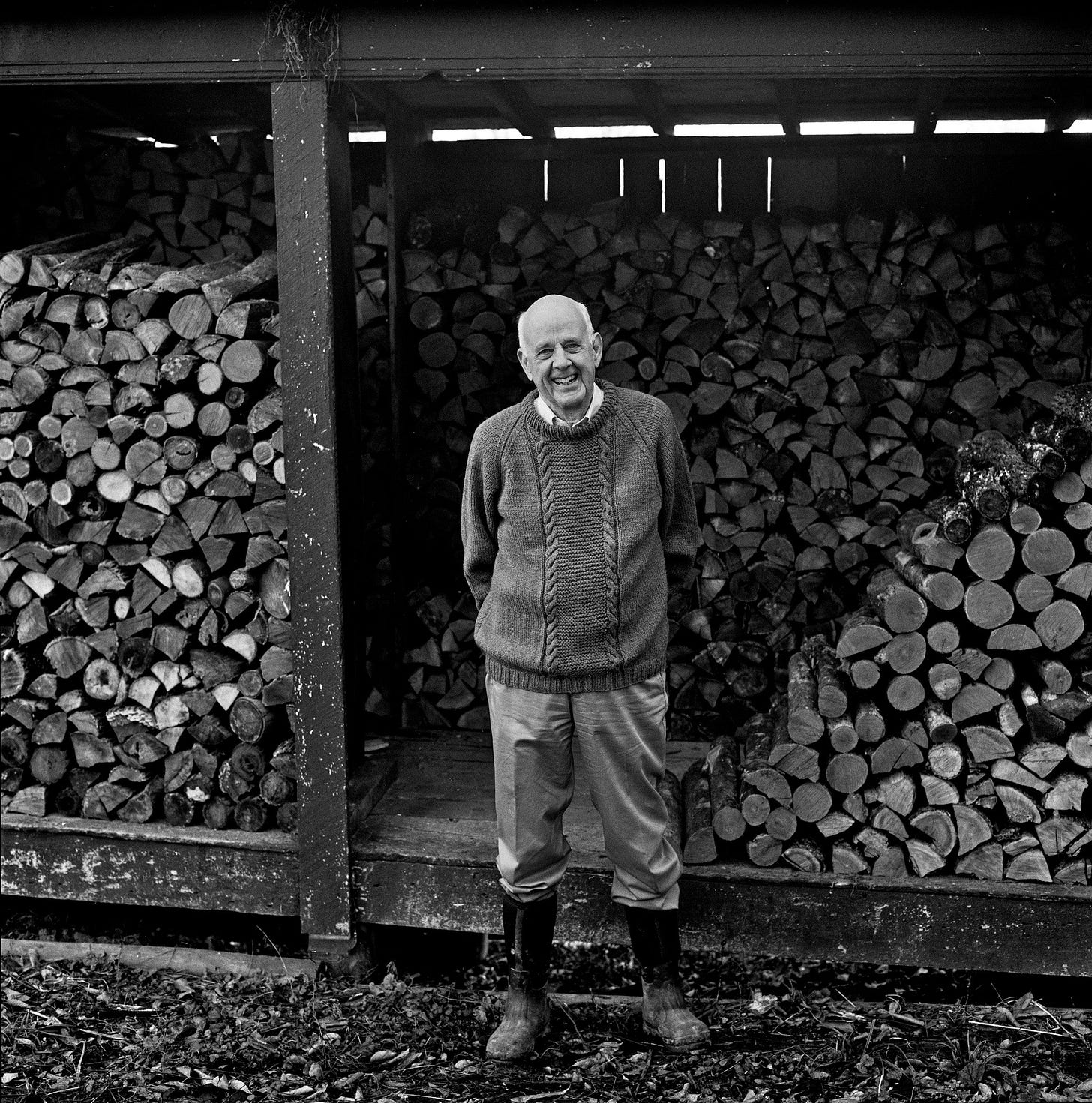 Wendell Berry stands by piles of firewood.