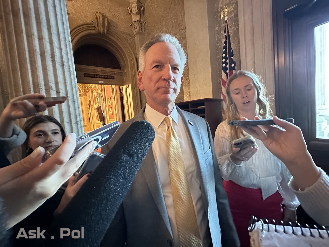 Reporters huddle around a Senator in a suit recording his responses to their questions. Photo: Matt Laslo for © www.askapolpolitics.com