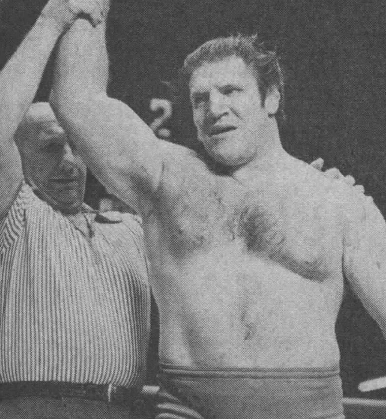 Bruno Sammartino, shirtless with dark hair, has his arm raised in victory by a referee in a striped shirt, in a 1973 black-and-white photo