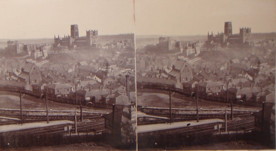 Historic sepia-toned photograph depicting a panoramic view of a town with numerous buildings and a prominent cathedral in the background.