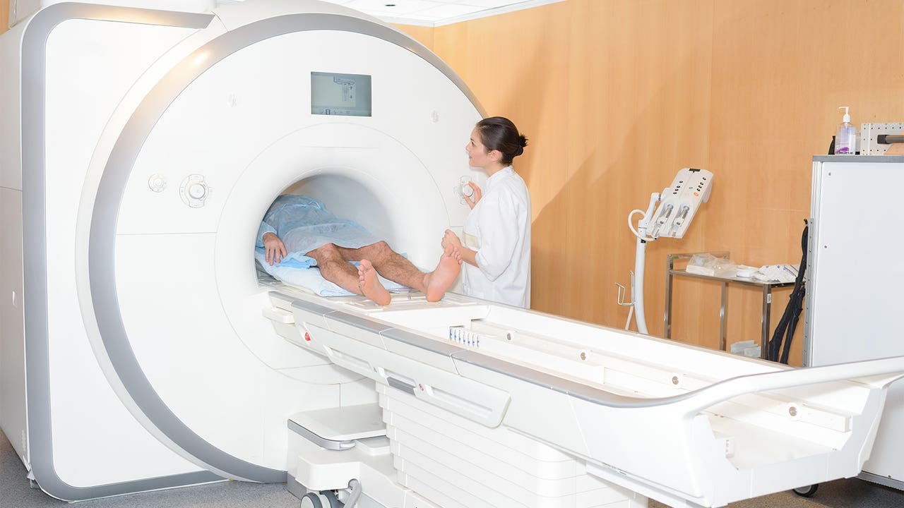 A photo of a female radiologist guiding her male patient into an MRI scanner.