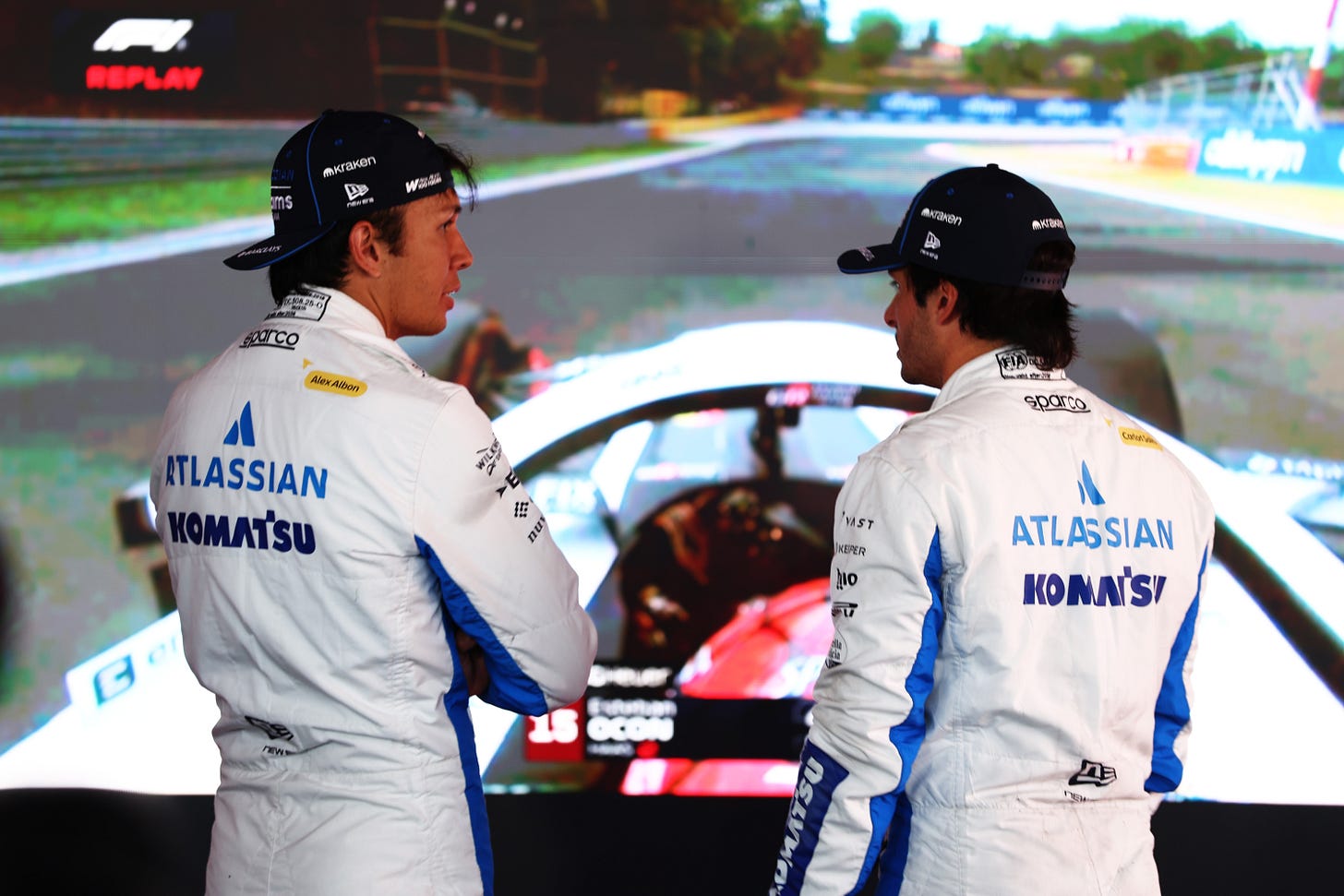 Alex Albon and Carlos Sainz in conversation with their backs to the camera while they watch on-board footage from a qualifying session in the TV pen