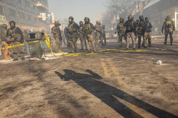 Armed and masked immigration agents stand in the street amid clouds of tear gas.