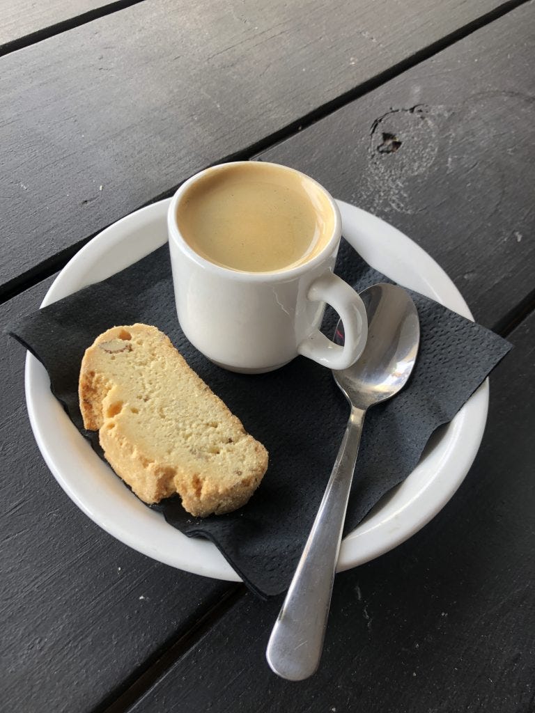 A demi-tasse of espresso sitting on a black napkin on a white saucer with a piece of biscotti and a silver spoon A demi-tasse of espresso sitting on a black napkin on a white saucer with a piece of biscotti and a silver spoon