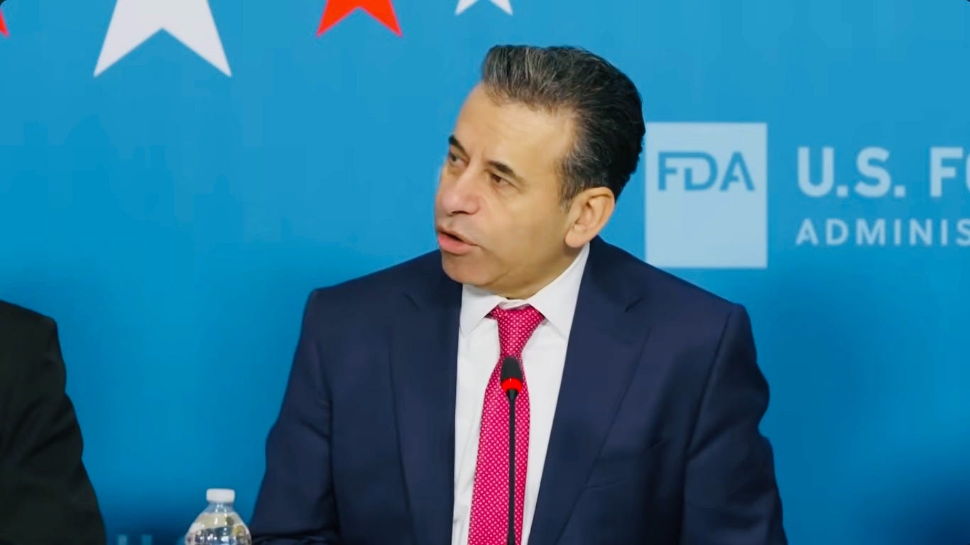 FDA Commissioner Dr. Marty Makary speaks at a microphone during an agency event, wearing a navy suit and pink tie. 