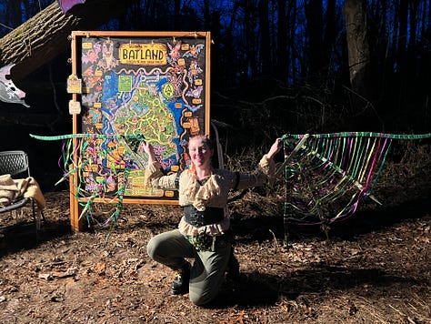 First image is a picture of an upright painted bat with pink ears hanging on a tree, second image is the entry way to the Batland Exhibit + Save the Woods party, next is a painted sign on fabric that reads KEEP ASHEVILLE GREEN, fourth is an image of the Batland Exhibit sign with Spencer Beals, my daughter, and me, fifth is a close up of the Batland Exhibit sign which is a map of the woods showing where the bats are placed- sixth is an image of a party goer with large homemade see- through bat wings posing in front of the sign, sevent is a home made painted sign that reads 'Chancellor to Helene "Hold My Beer! Watch Me Take All the Trees!" eight is an image of Spencer's painting titled "Eyes of Appalachia" and finally we have a hand made carrier pigion on a tree as part of the exhibit.