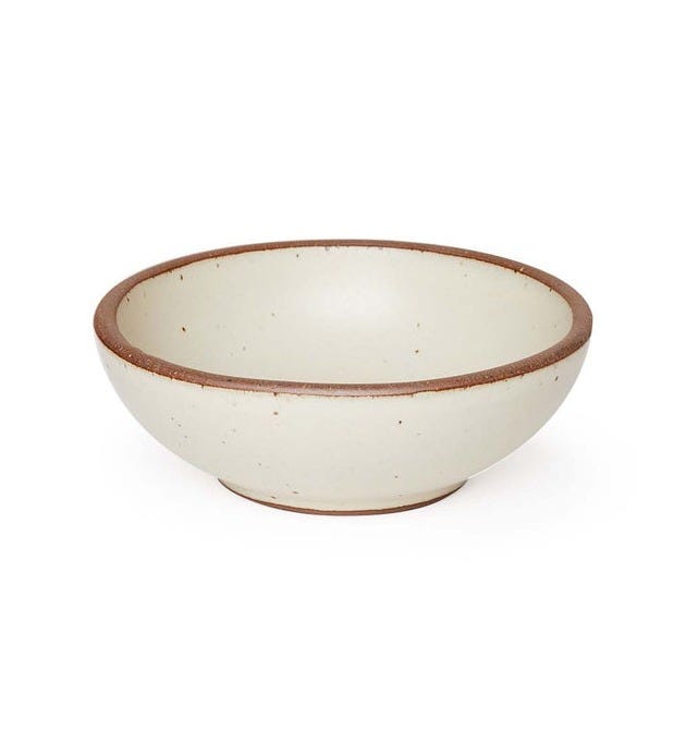 A small shallow ceramic bowl in a warm, tan-toned, off-white color featuring iron speckles and an unglazed rim A small shallow ceramic bowl in a warm, tan-toned, off-white color featuring iron speckles and an unglazed rim