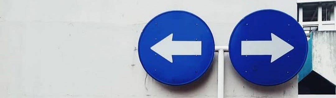 Two blue signs pointing in opposite directions on a white wall