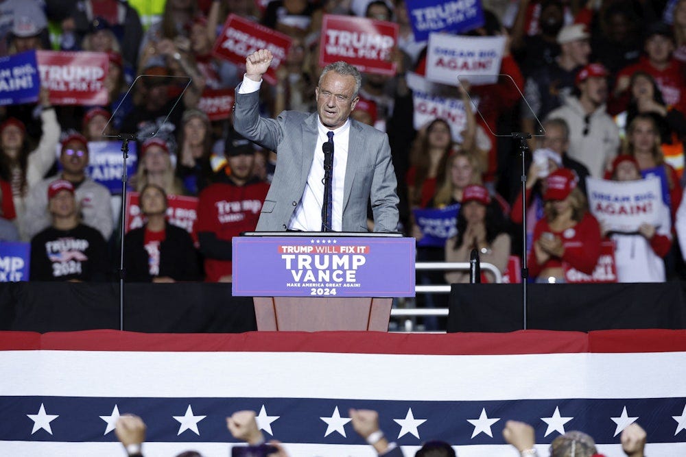 RFK Jr raises his fist while standing at a podium, with fans behind him.