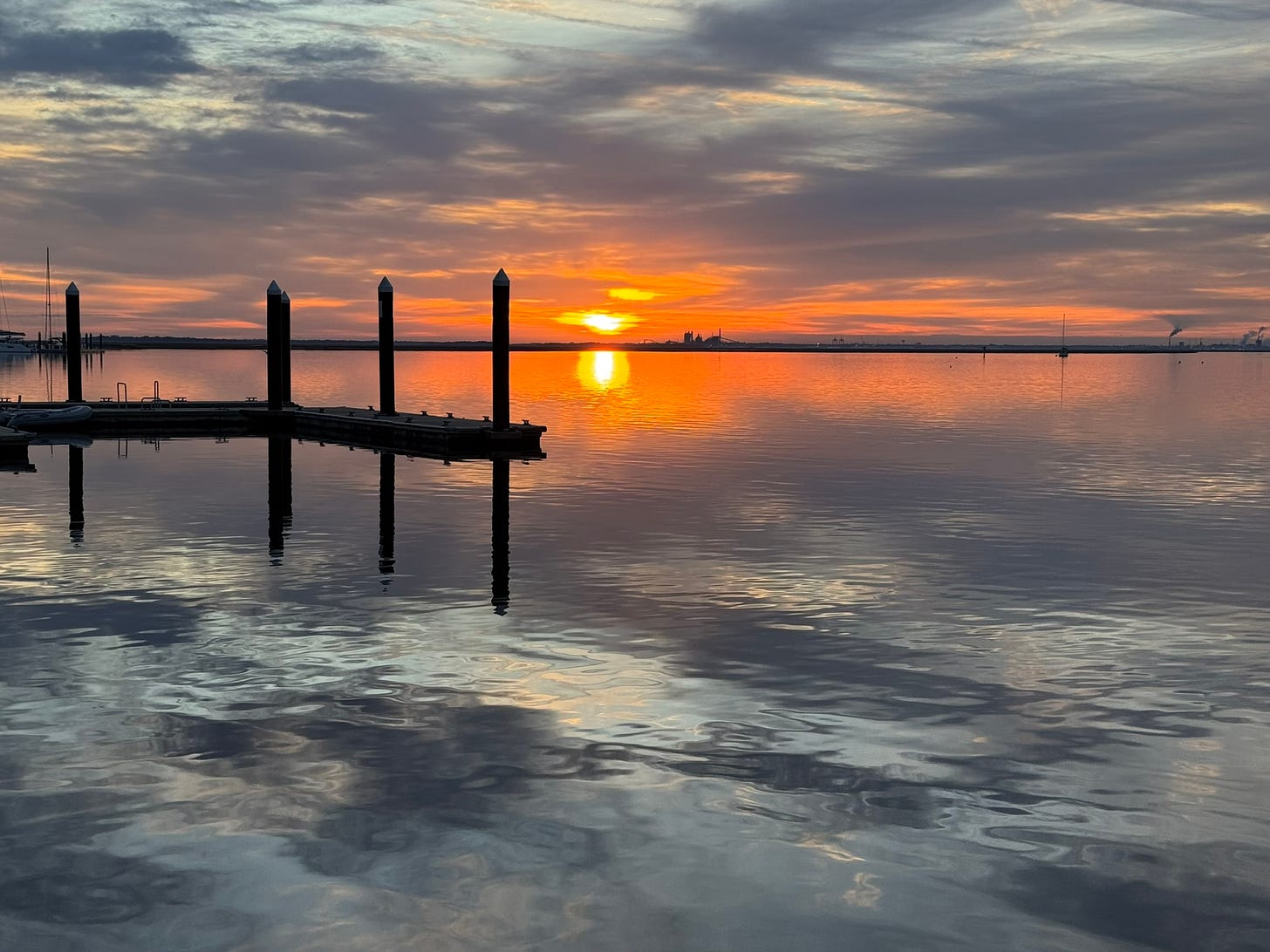The orange sun rising over the river with a dock in the foreground 