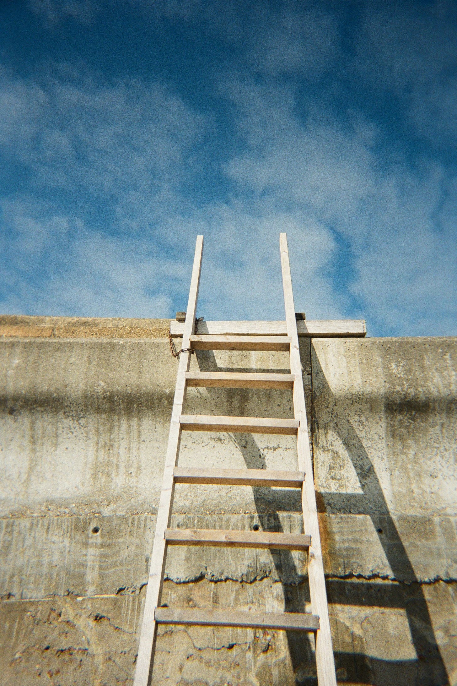 photo of a ladder in place to climb a wall and reach the blue sky beyond photo of a ladder in place to climb a wall and reach the blue sky beyond