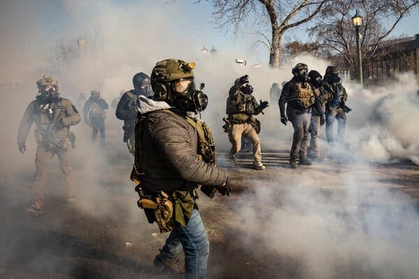 People in helmets and gas masks stand amid tear gas on a street.