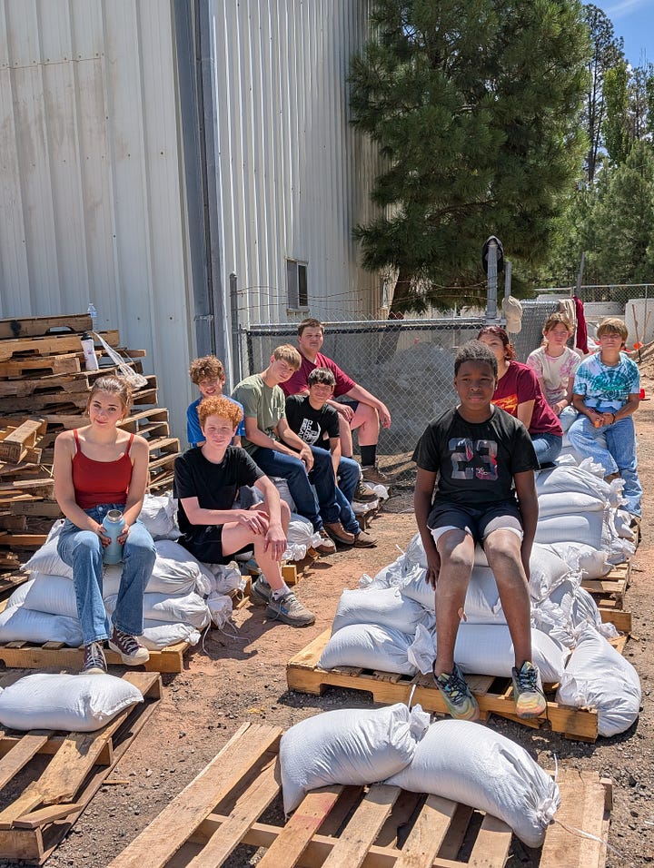 children fill hygeine and food bags with relief organizations. Children sit on sand bags outdoors