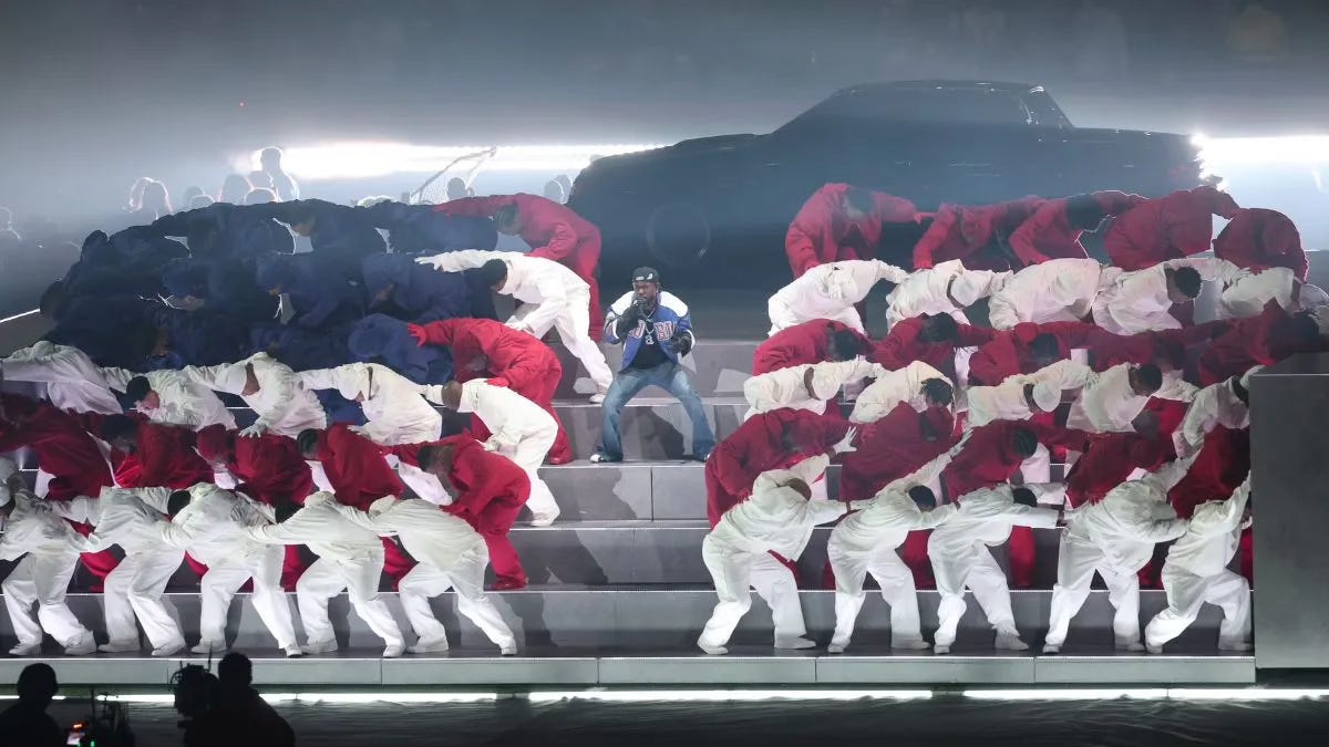 Kendrick Lamar performing at Super Bowl LIX with dancers surrounding him in the formation of an American flag split down the middle.