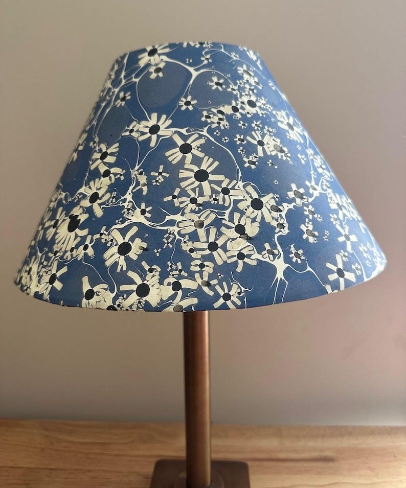 May include: A blue lampshade with a white floral pattern. The lampshade is cone-shaped and has a white base.