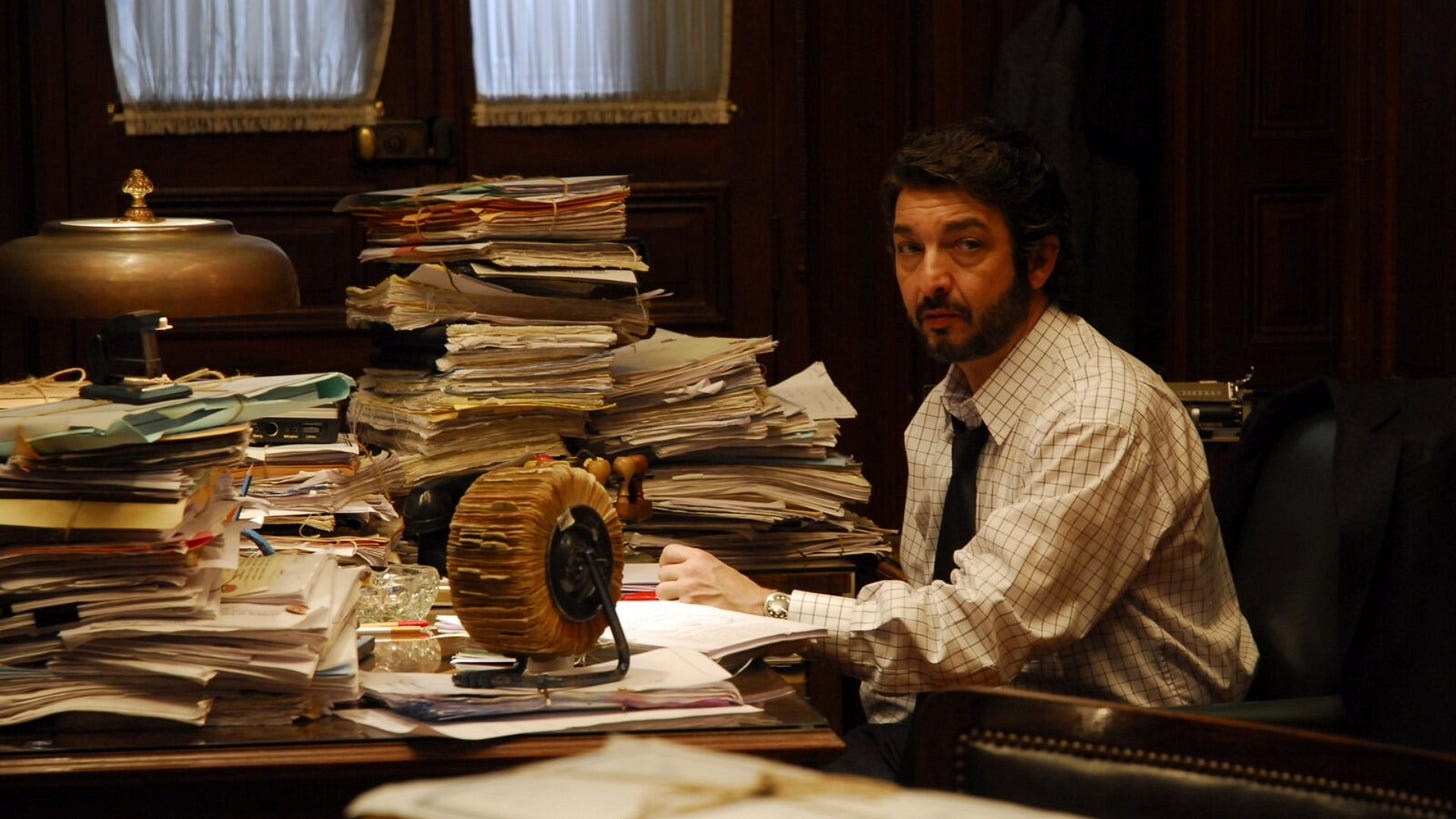 The Secret in Their Eyes | Still features Ricardo Darín as Benjamin Esposito seated at a messy desk.