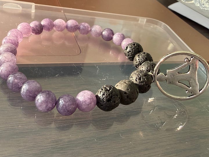 Two bracelets with lavender colored stones and lava rock. One has a shiny bead and the other a yoga charm.