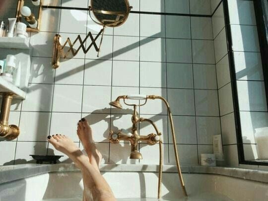 This may contain: a person's bare feet in a bathtub with white tile and gold fixtures This may contain: a person's bare feet in a bathtub with white tile and gold fixtures