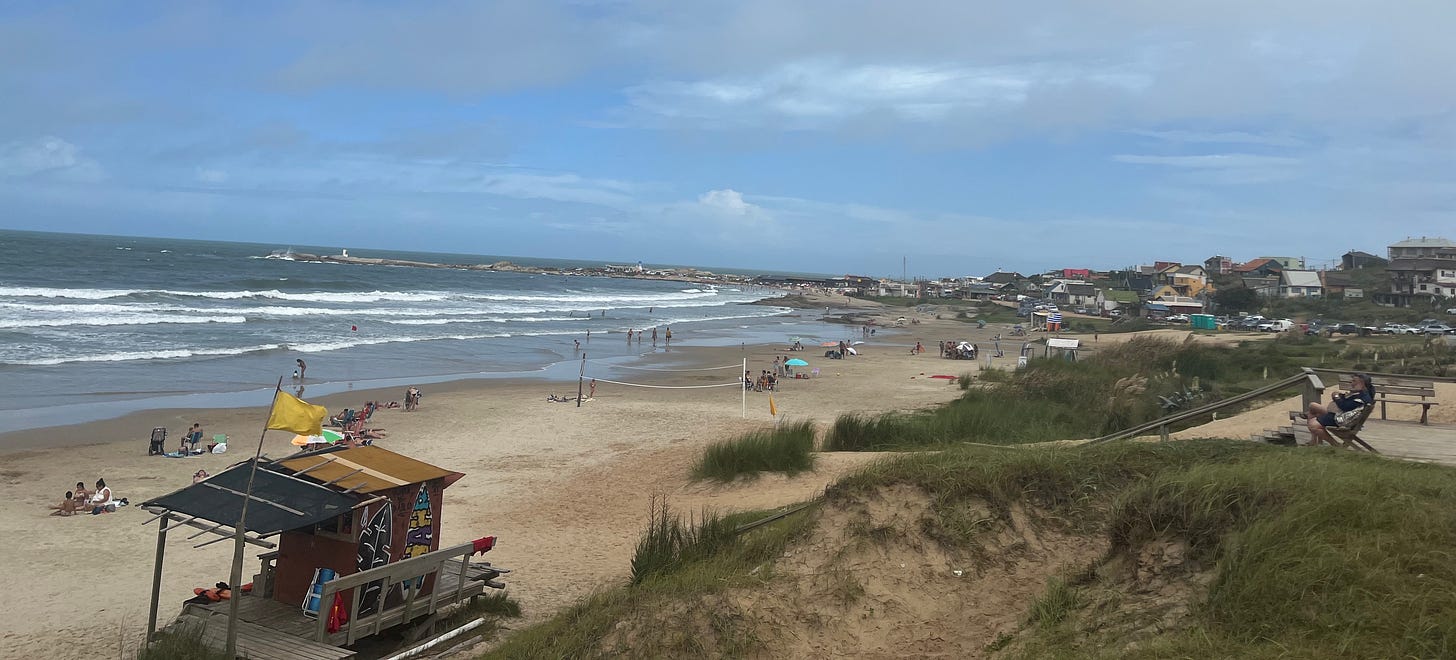 a calm beach with lifeguard station and people sitting in the sand in Punta del Diablo a calm beach with lifeguard station and people sitting in the sand in Punta del Diablo