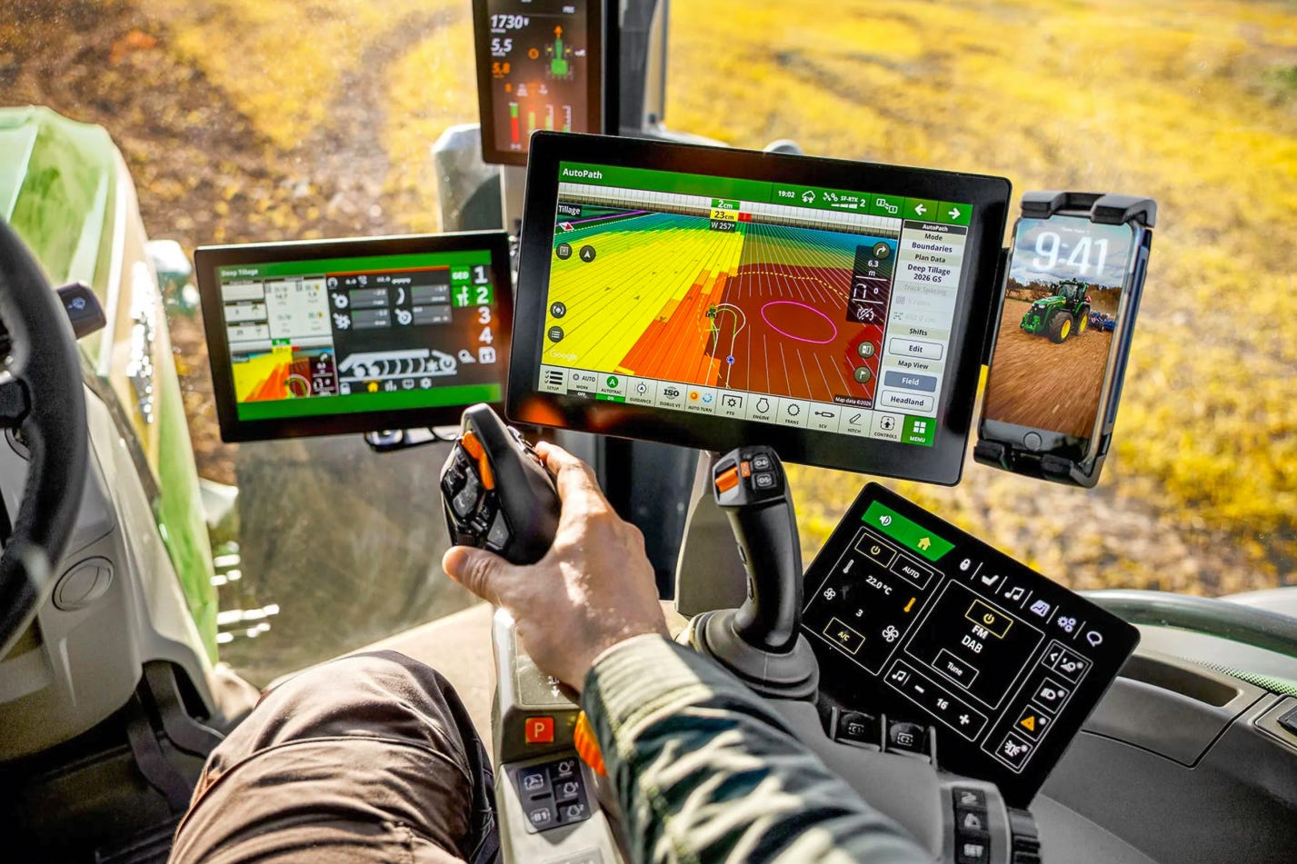 Innenansicht einer modernen Traktorkabine von John Deere mit vier digitalen Bildschirmen für Präzisionslandwirtschaft. Der Fahrer hält den Fahrhebel, während auf dem grossen Hauptmonitor eine farbige Feldkarte mit Fahrspuren und Autosteer-Anzeige läuft. Daneben zeigen weitere Displays Maschinenparameter. Innenansicht einer modernen Traktorkabine von John Deere mit vier digitalen Bildschirmen für Präzisionslandwirtschaft. Der Fahrer hält den Fahrhebel, während auf dem grossen Hauptmonitor eine farbige Feldkarte mit Fahrspuren und Autosteer-Anzeige läuft. Daneben zeigen weitere Displays Maschinenparameter.