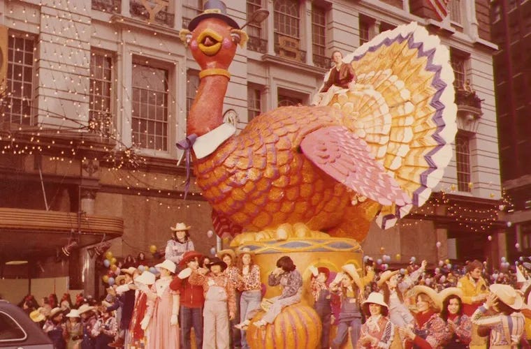 A vintage Macy's thanksgiving day parade. there are a lot of people dressed in cowboy costumes surrounding and riding on a turkey float. I'm guessing this is from the 70s.