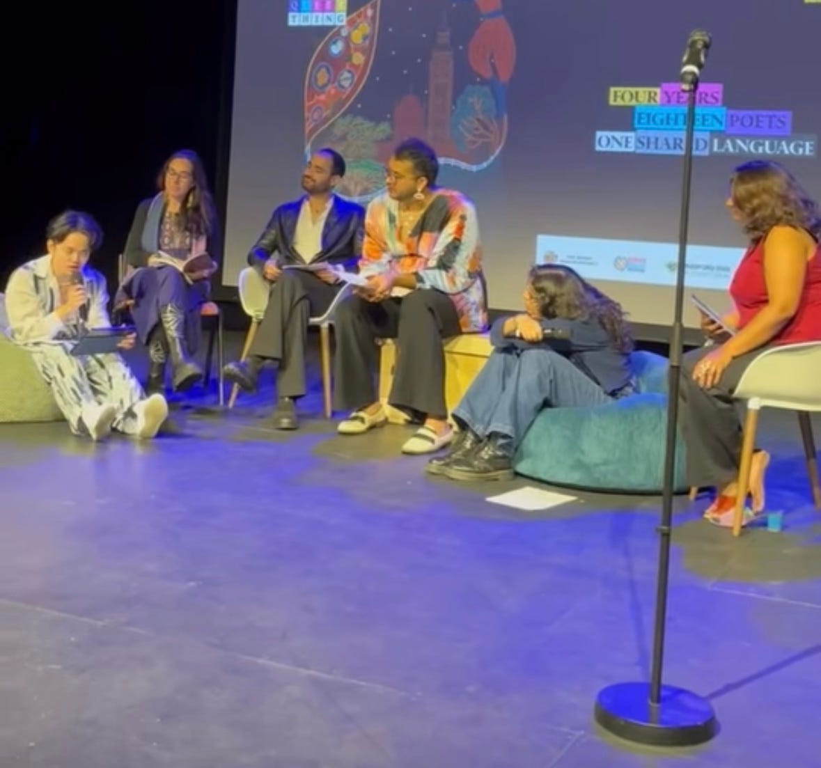 the six poets from language is a queer thing clustered on chairs, bean bags, and apple boxes on stage. we are all watching mukahang speak with rapt attention.