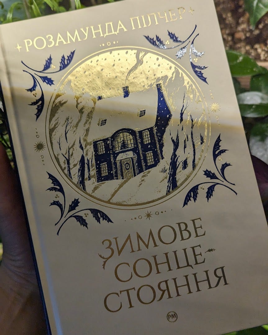 На зображенні жіноча рука тримає книжку з написом 'Зимове сонцестояння'. Автор книги Розамунда Пілчер. Видавництво РМ.