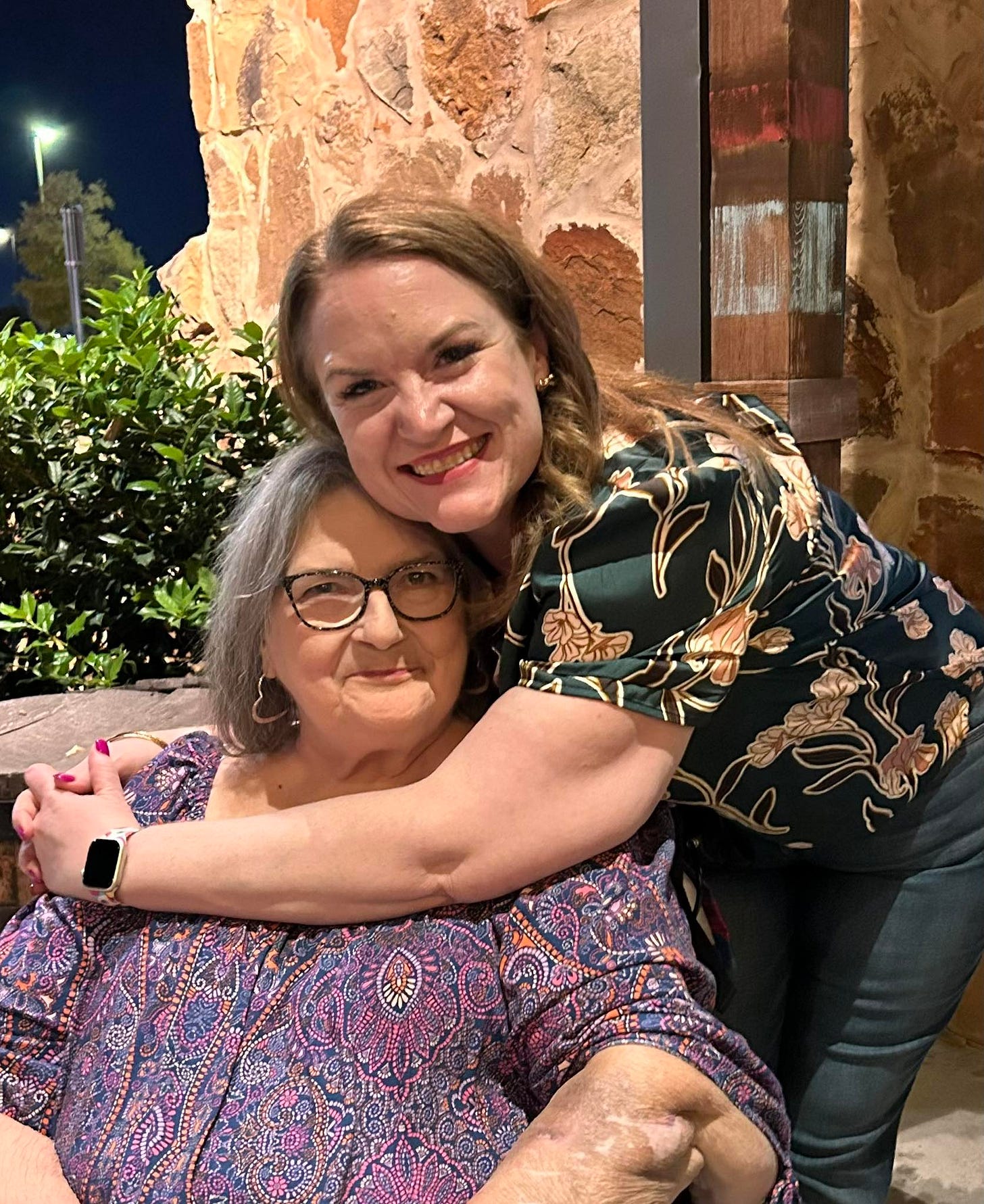 My mom and sister Jessica pictured with Mom sitting and Jessica standing with her arm around Mom's shoulders.