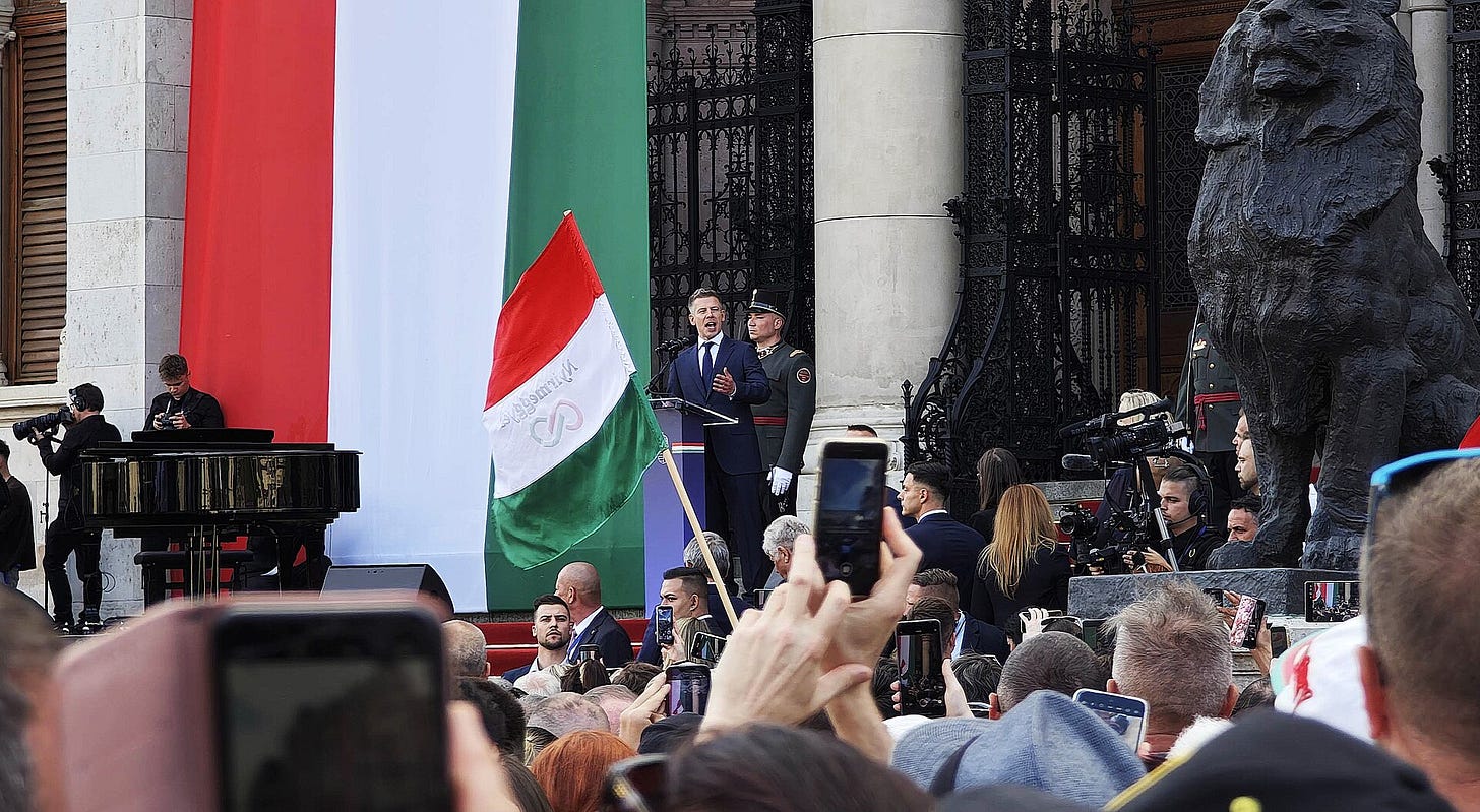 Péter Magyar speaking outdoors at Kossuth Square in Budapest, surrounded by supporters and Hungarian flags. Péter Magyar speaking outdoors at Kossuth Square in Budapest, surrounded by supporters and Hungarian flags.