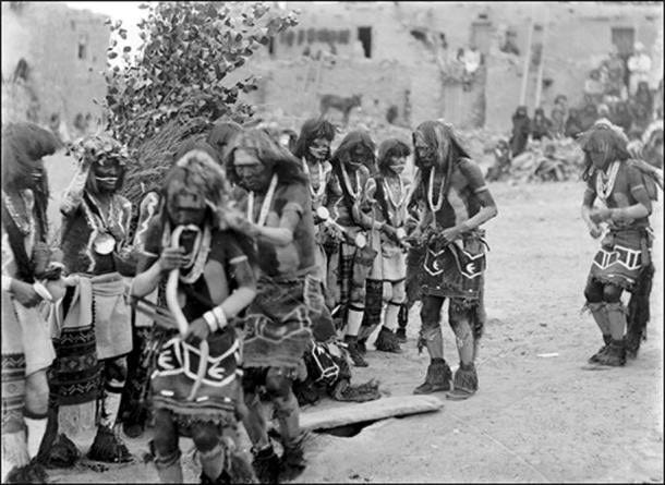 Front row, Snake dancers near foot-drum, Oraibi village, Third Mesa, 1898, next row Antelope dancers, one with cottonwood wreath, medicine bowl, and water-sprinkler. Kisi (leaves of “snake house”) in the background. Front row, Snake dancers near foot-drum, Oraibi village, Third Mesa, 1898, next row Antelope dancers, one with cottonwood wreath, medicine bowl, and water-sprinkler. Kisi (leaves of “snake house”) in the background.