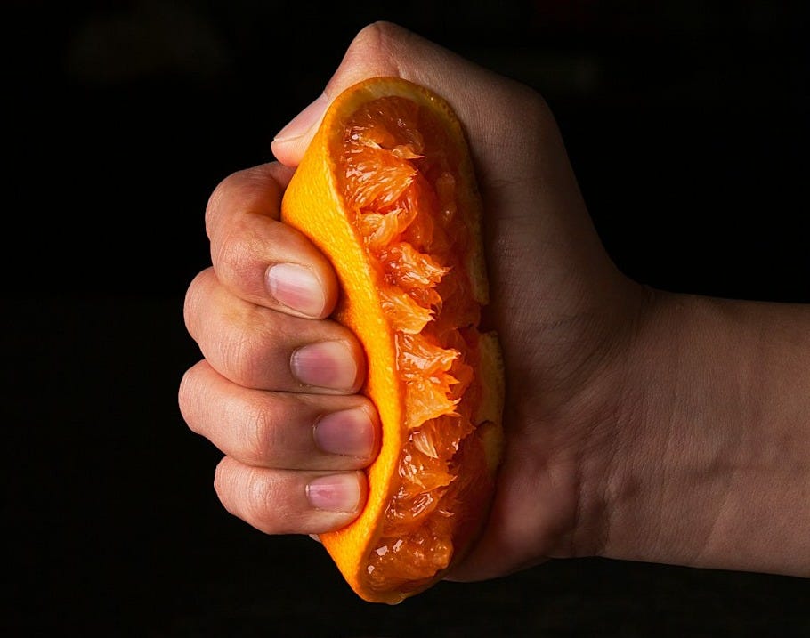 person holding orange fruit beside clear drinking glass with red liquid