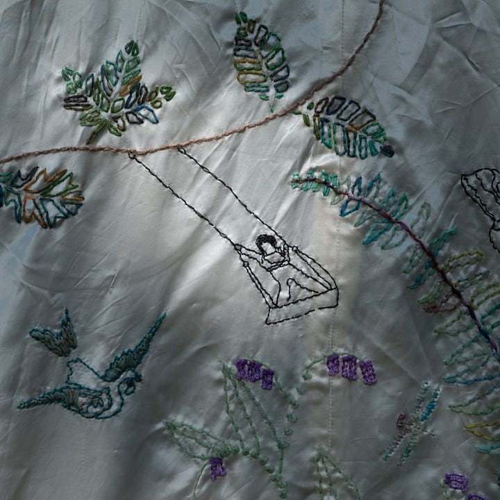 A diptych. On left, a young person is embroidered swinging on a swing, surrounded by multi-colored embroidered leaves and a bird; On the right, a reflection of a person on a wet beach, their reflected arms raised, merging with bubble covered seaweed.