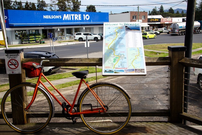 An orange bike is propped up against a mounted map of the town of Bermagui. An orange bike is propped up against a mounted map of the town of Bermagui.