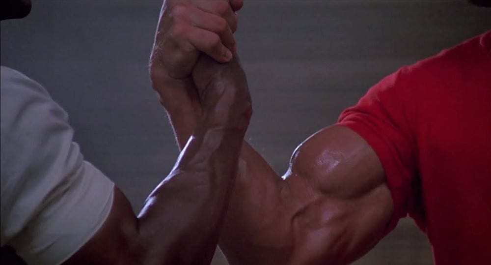 a still from the movie predator: arnold schwarzenegger & carl weathers' homoerotic bro team handshake of meme legend