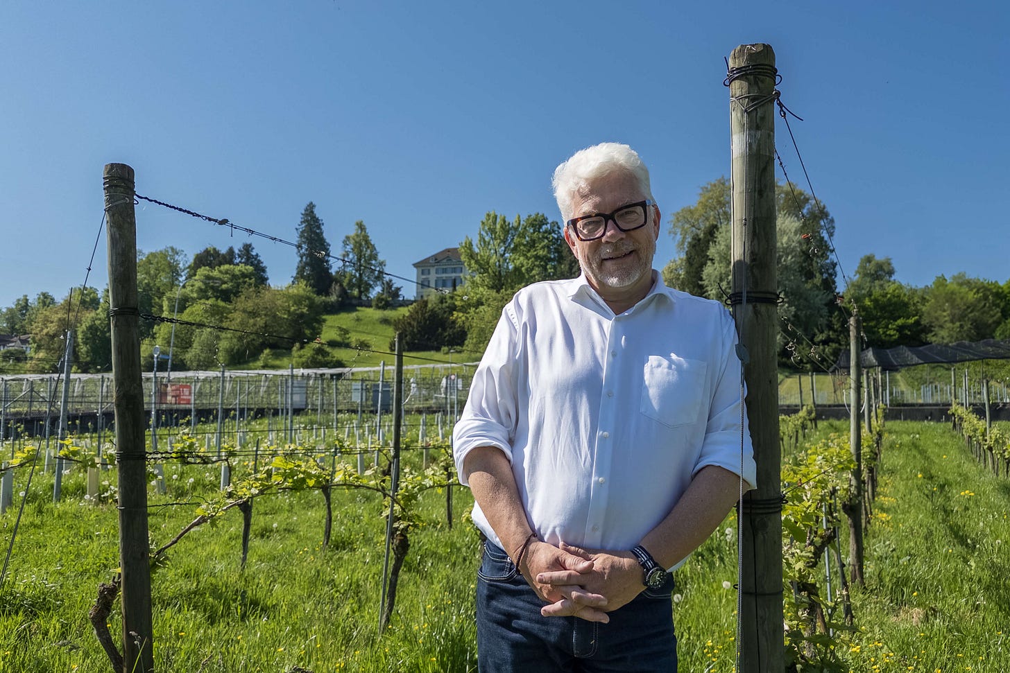 Der Leiter des Weinbauzentrums Wädenswil, Martin Wiederkehr, steht in einem sonnigen Rebberg am Zürichsee – im Hintergrund das Forschungsareal mit Rebanlagen und das historische Schlösschen auf dem Hügel.