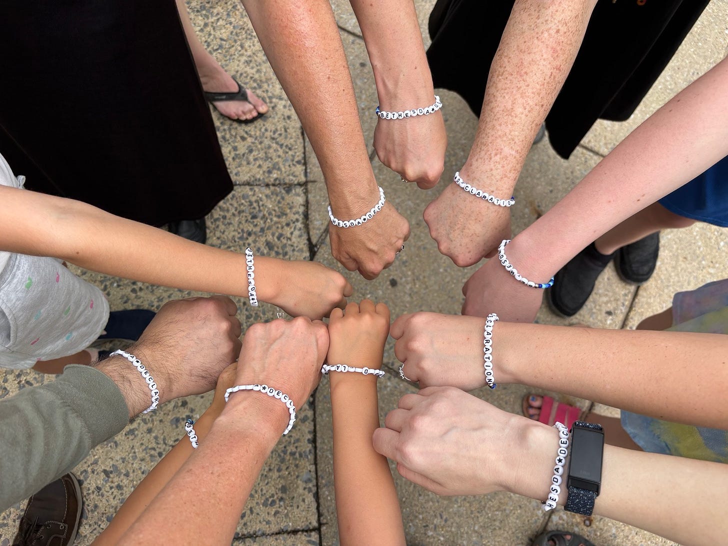 A photo a several arms wearing Bethesda Declaration bracelets with hands put into the center. 